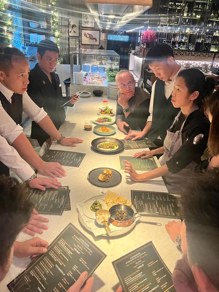 Tammie at a long kitchen pass with chefs and printed menus