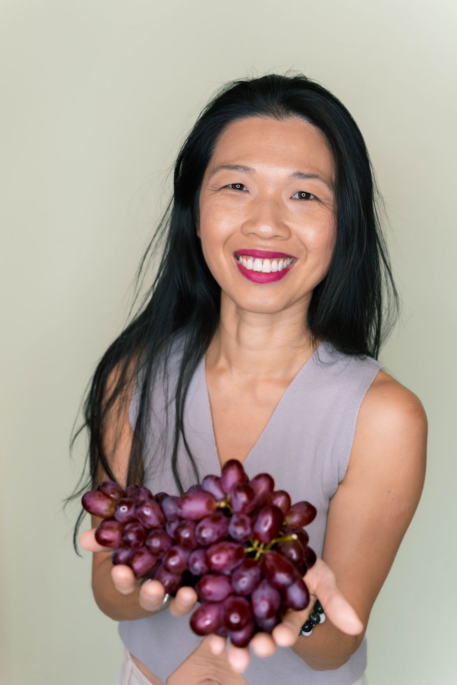 Tammie smiling, holding a bunch of red grapes out in both hands