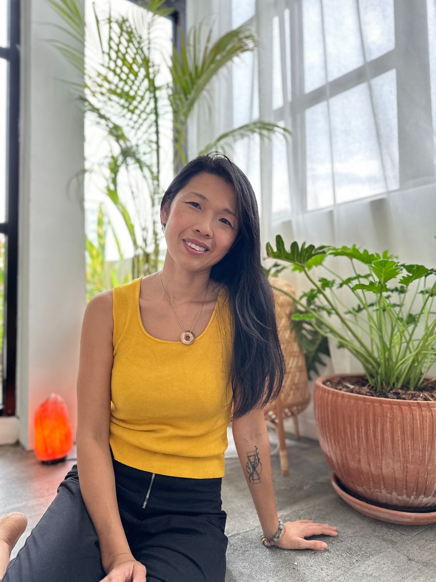 Tammie smiling, sitting by a window with plants, in a yellow top