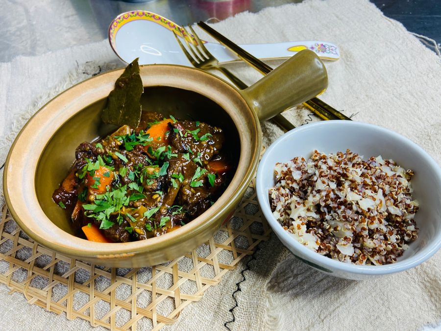 A braised dish in a clay pot with a bowl of mixed grains
