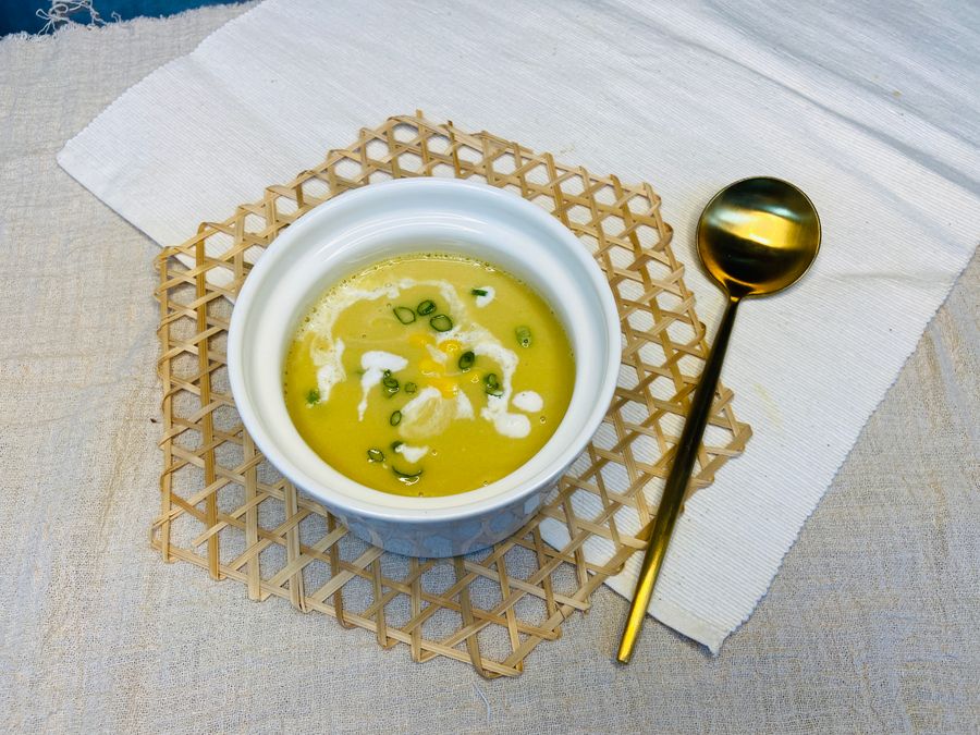 A bowl of golden soup on a woven gold placemat