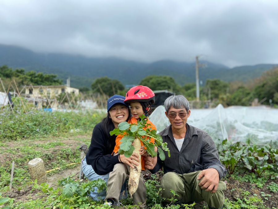 Tammie in a vegetable field with a farmer and a child, holding fresh greens