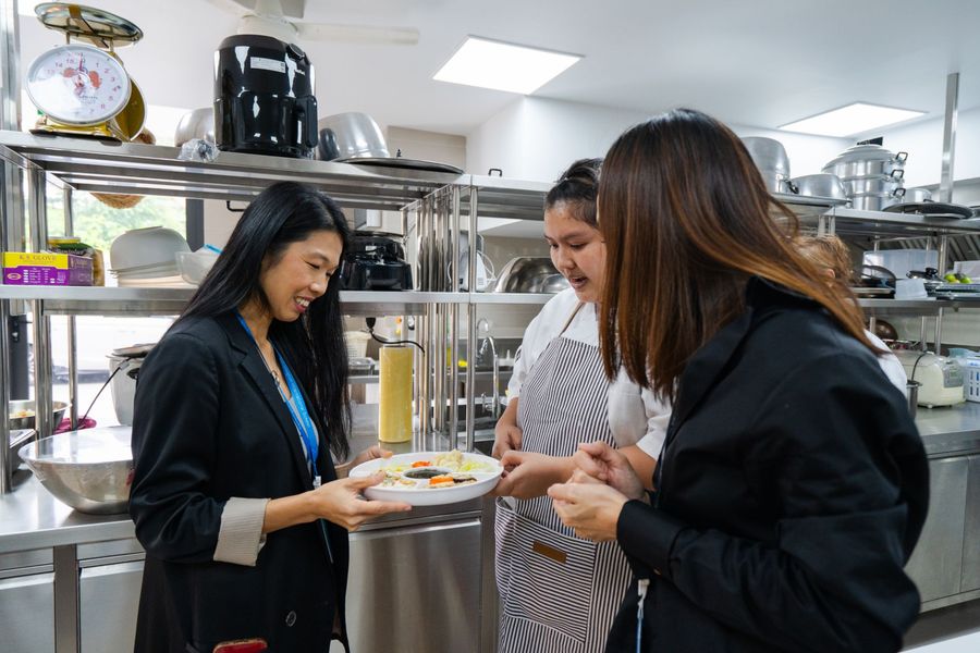 Tammie in a school kitchen, holding a plate with a cook and a colleague