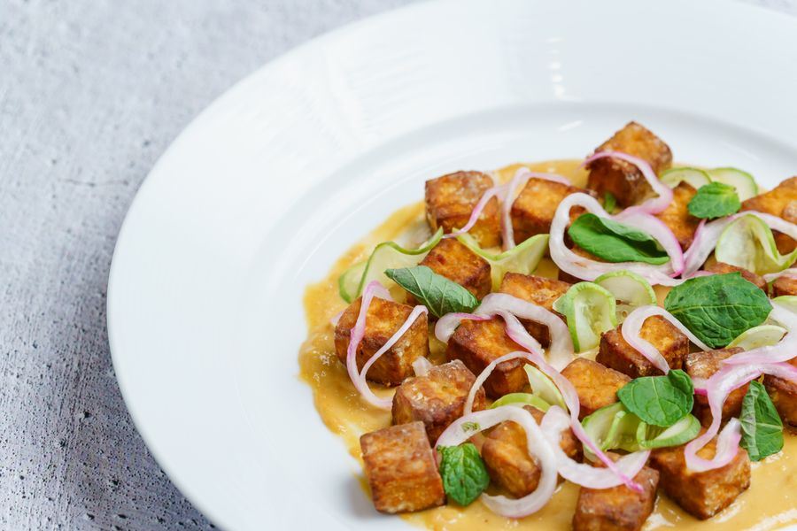 Crisp tofu cubes with herbs and shallots on a white plate